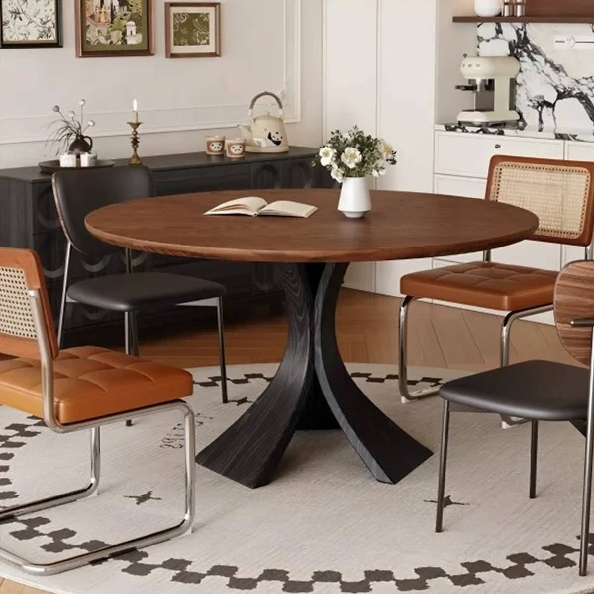 Round dining table with a dark base and mixed leather and cane chairs, set on a patterned rug.