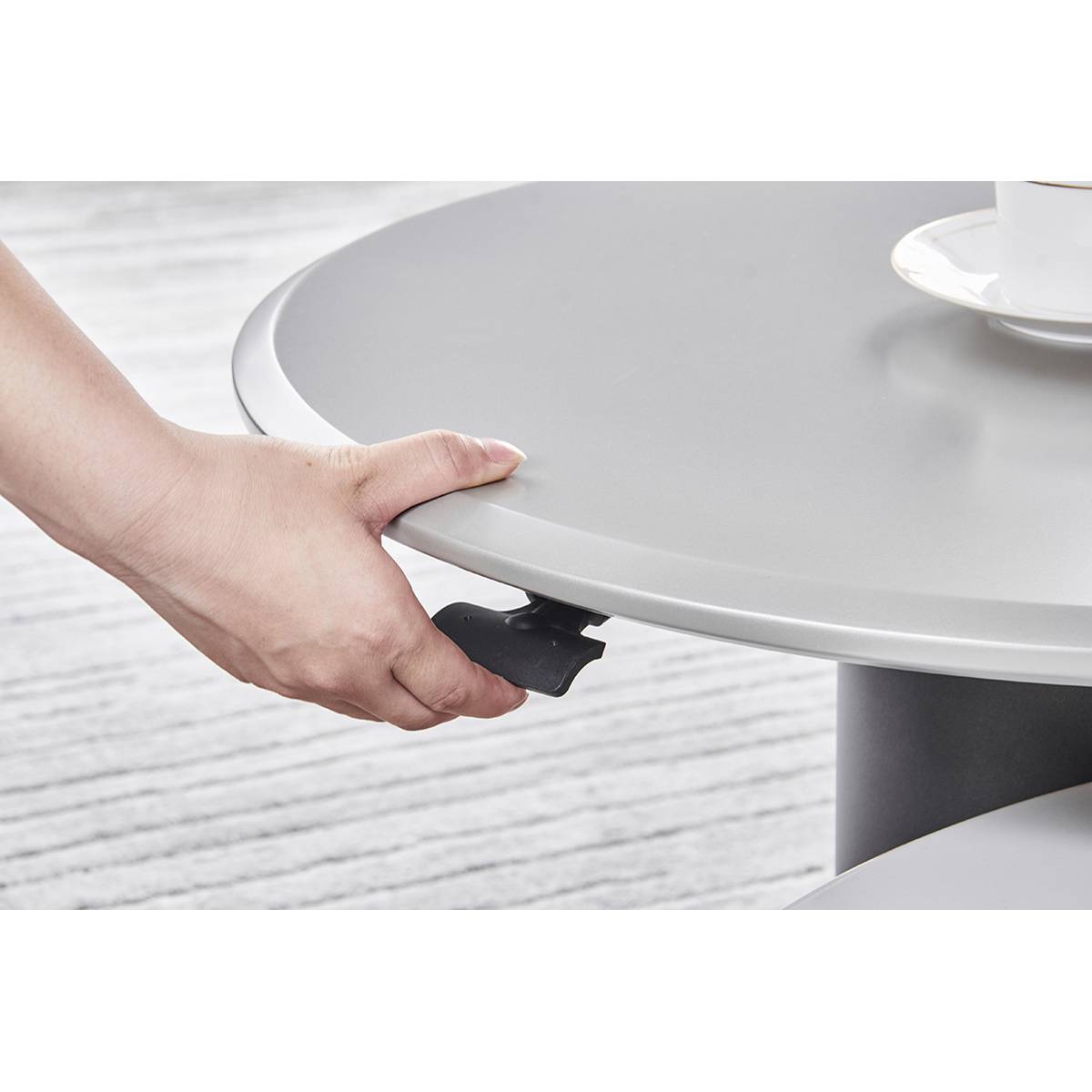 Hand operating the black handle mechanism to adjust the height of the smaller table.