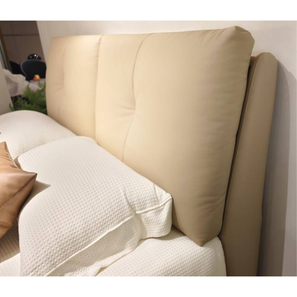 Close-up view of a beige upholstered bed headboard with white bedding