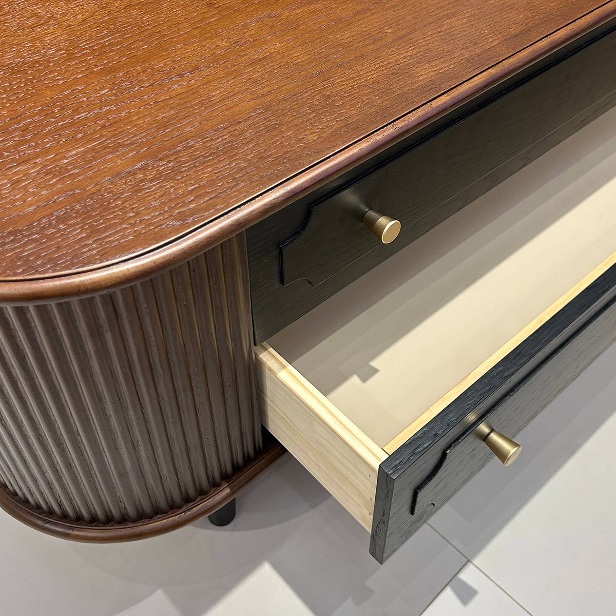 Close-up view of the coffee table showing the curved fluted side panel, dark wood drawer front, and brass knob.