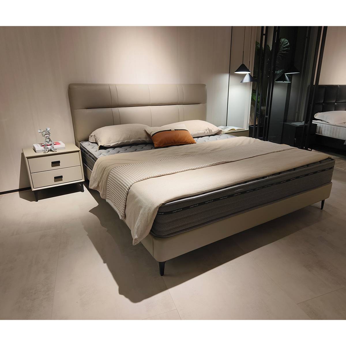 Side view of the beige leather soft bed with a grey mattress and orange accent pillow