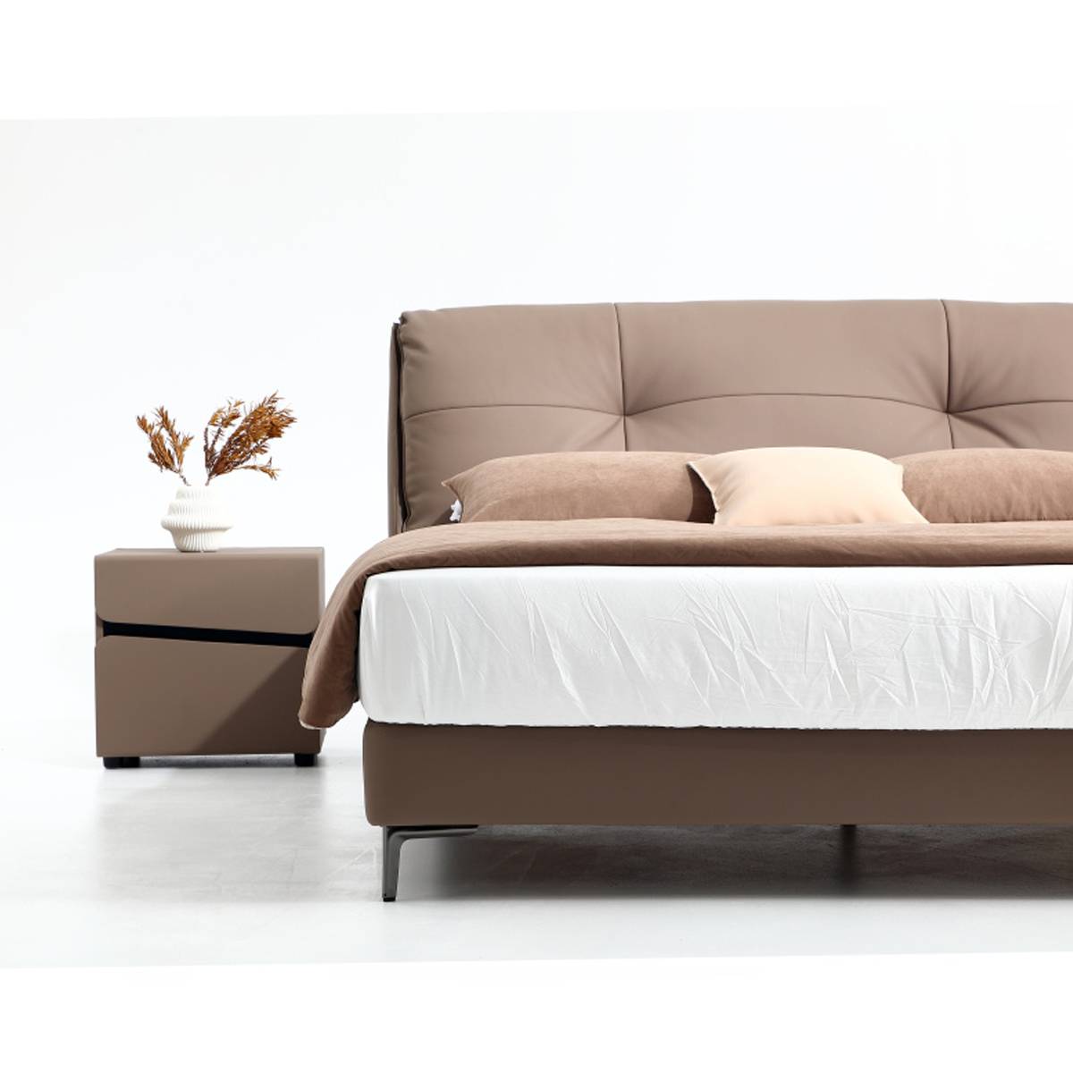 Full view of the brown leather soft bed with a matching bedside table and dried flower vase