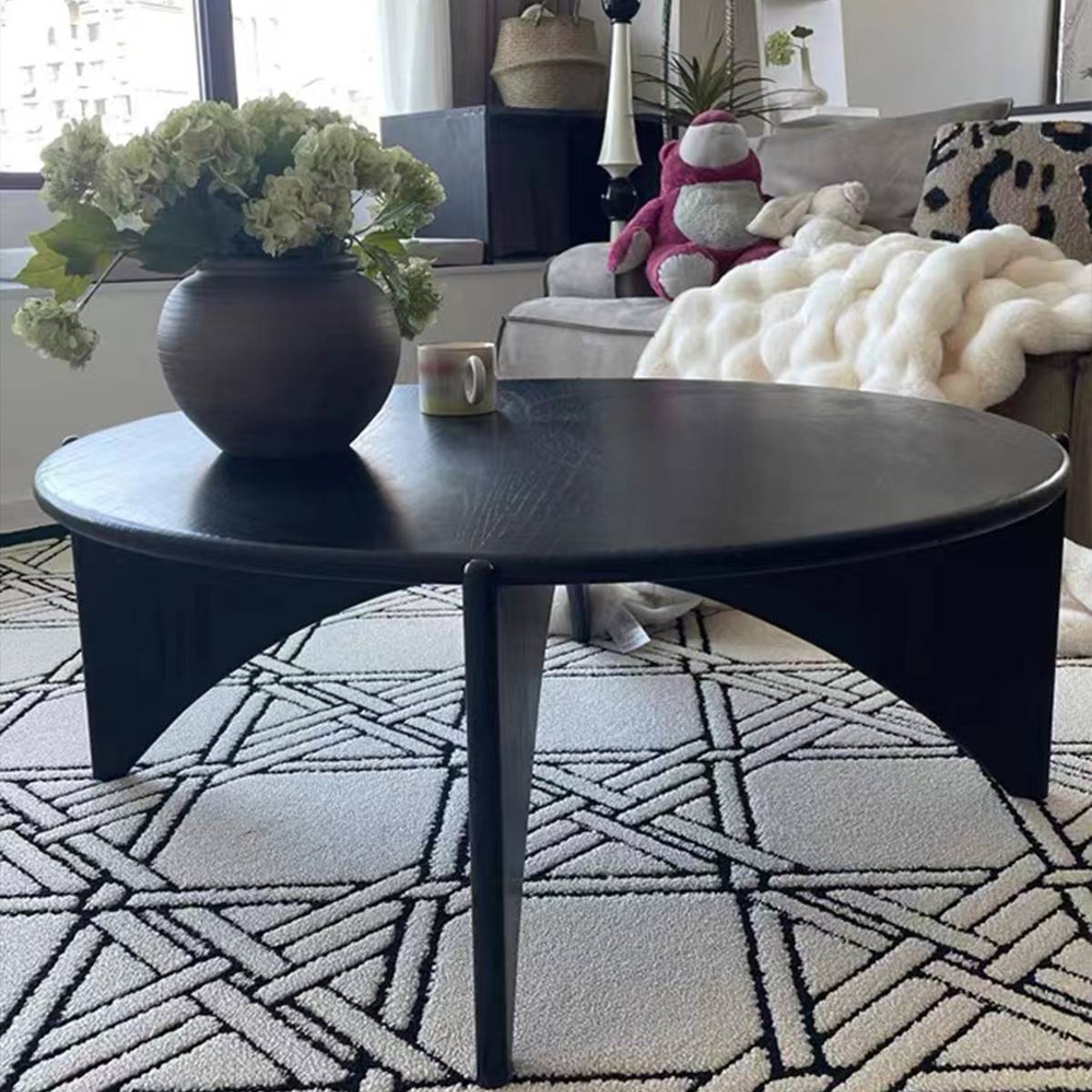 Black round coffee table with sculptural legs on a geometric rug