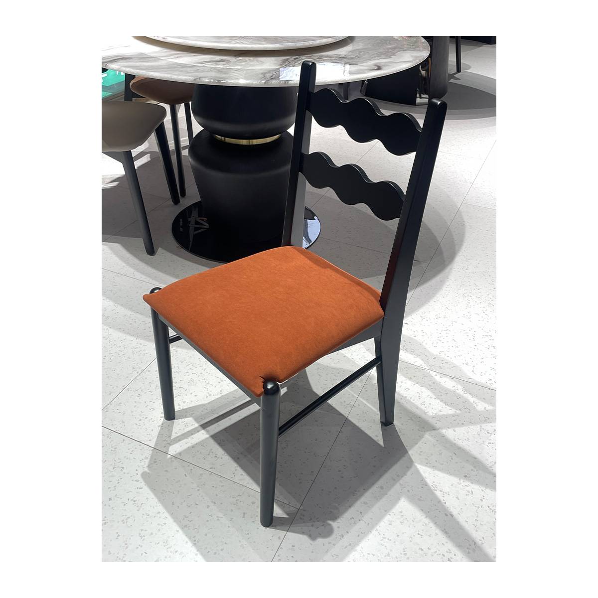 Front view of black mid-century dining chair with orange velvet seat