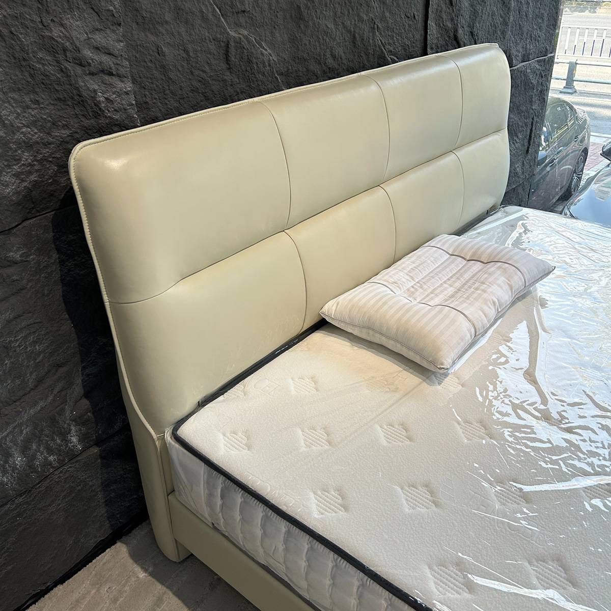 Full view of the cream-colored leather bed with a segmented headboard and mattress