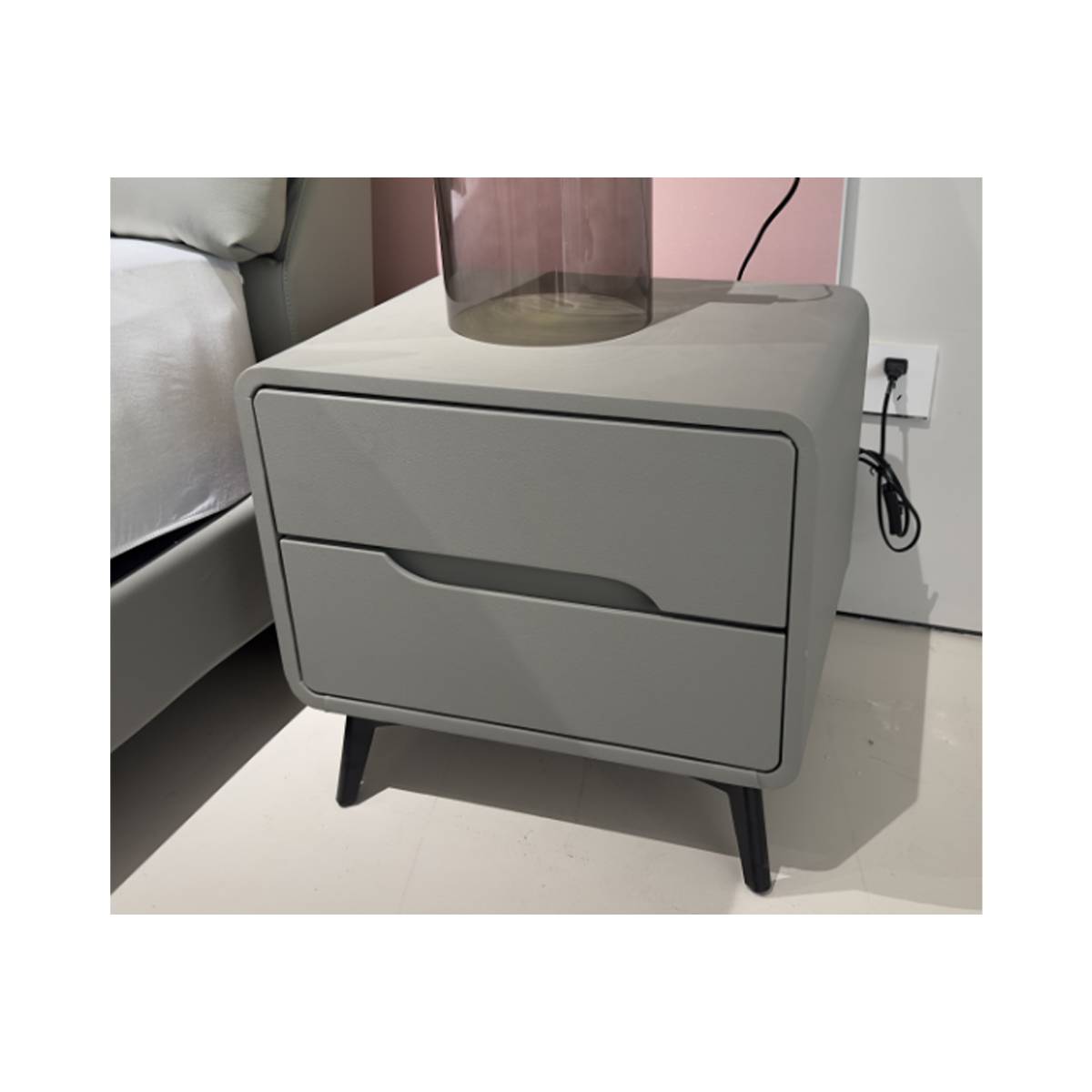 Close-up view of the bedside table next to a bed, showing drawer details and texture