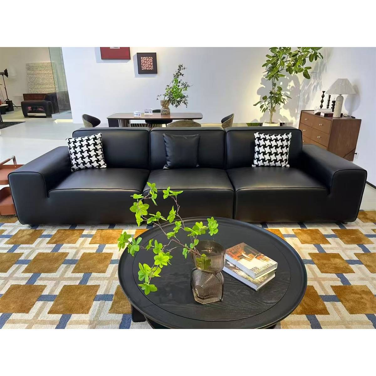 Black leather sofa with patterned throw pillows in a showroom setting with a round coffee table.