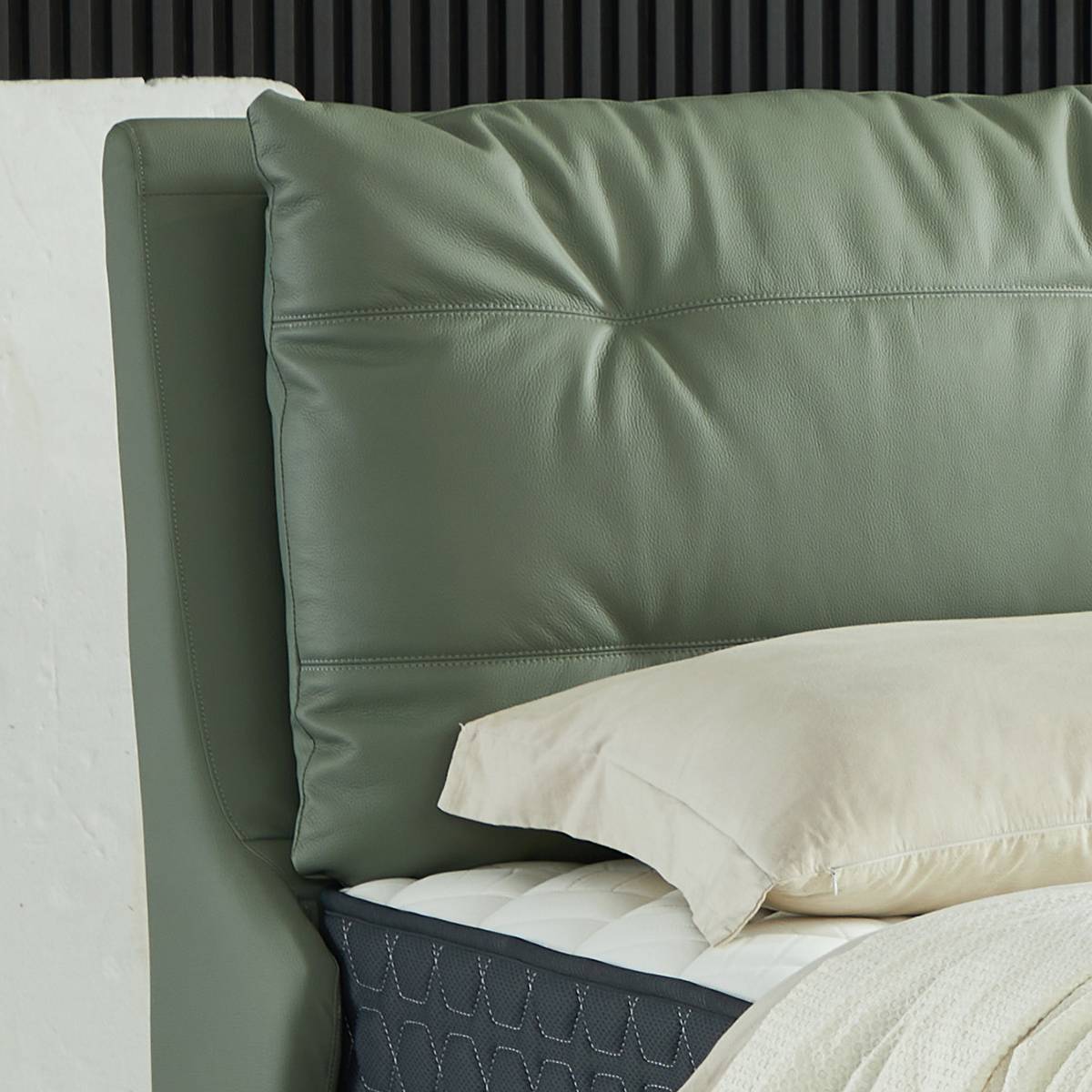 Close-up of a sage green leather bed headboard with tufted stitching and a white pillow