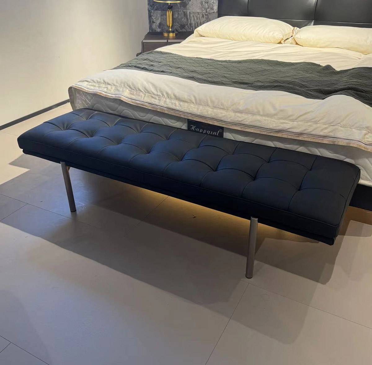 Angled view of the blue tufted bed bench showing the seat texture and metal legs.