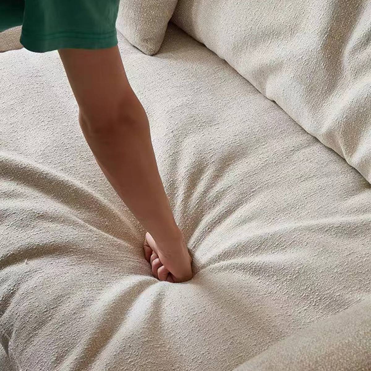 Close-up of a hand pressing into the seat cushion of a beige linen sofa to demonstrate firmness
