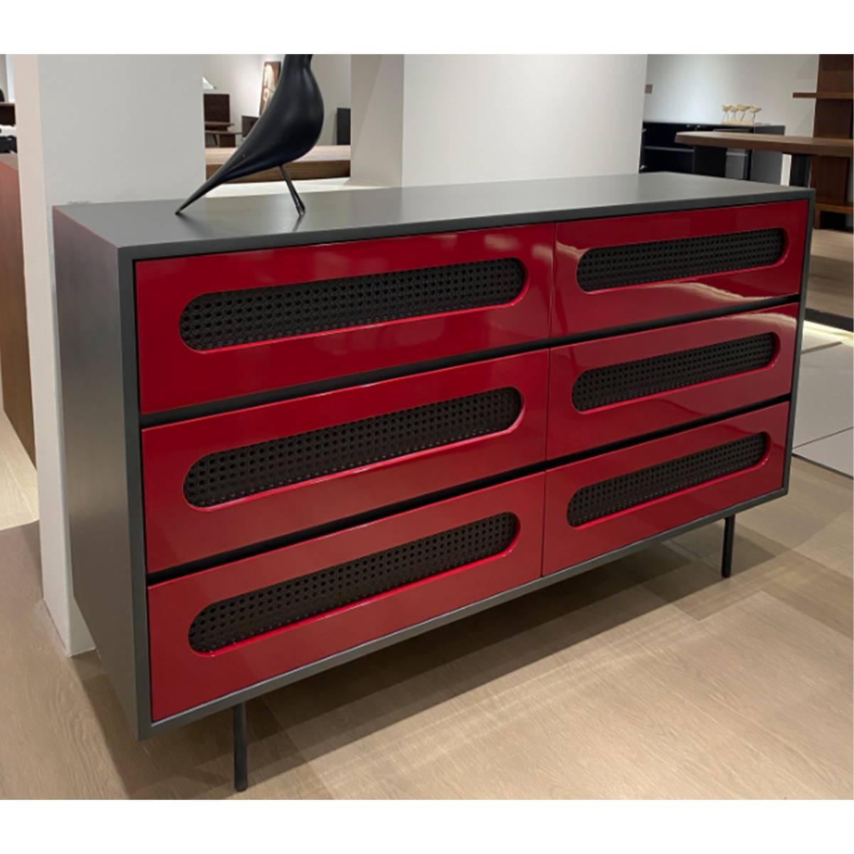 Angled view of a red sideboard with black frame and rattan inlay drawers in a showroom