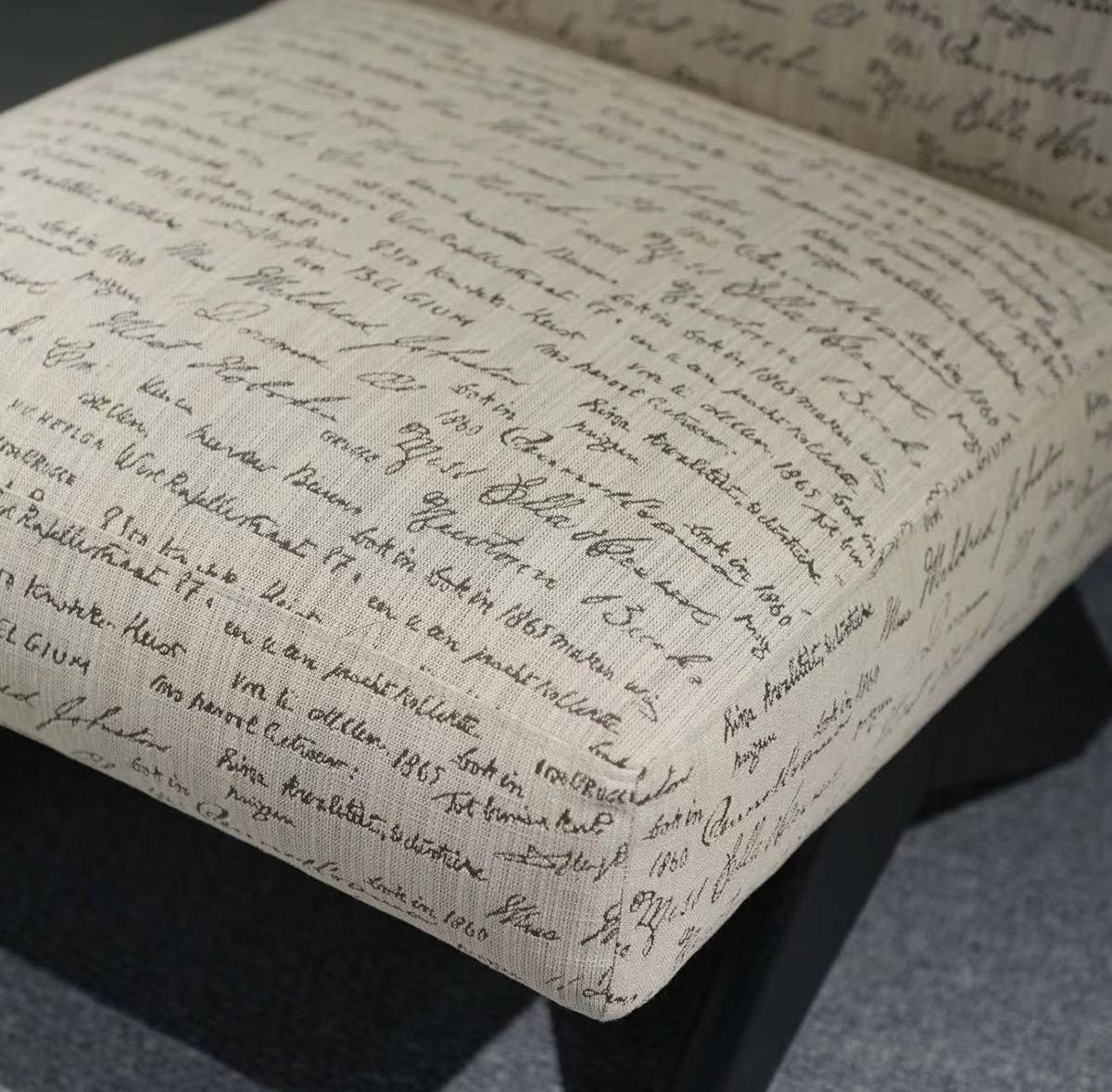Close-up of the chair seat showing the off-white fabric with black handwritten script pattern