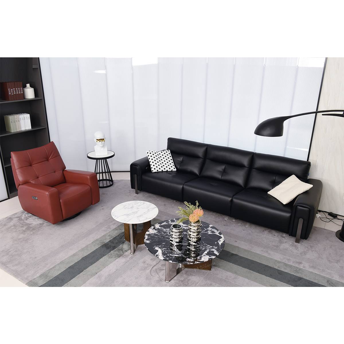 Wide view of the living room setup including the black sofa, a red recliner, and shelving unit