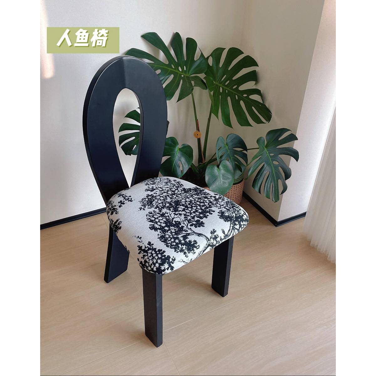 Black Mermaid dining chair with patterned seat next to a Monstera plant
