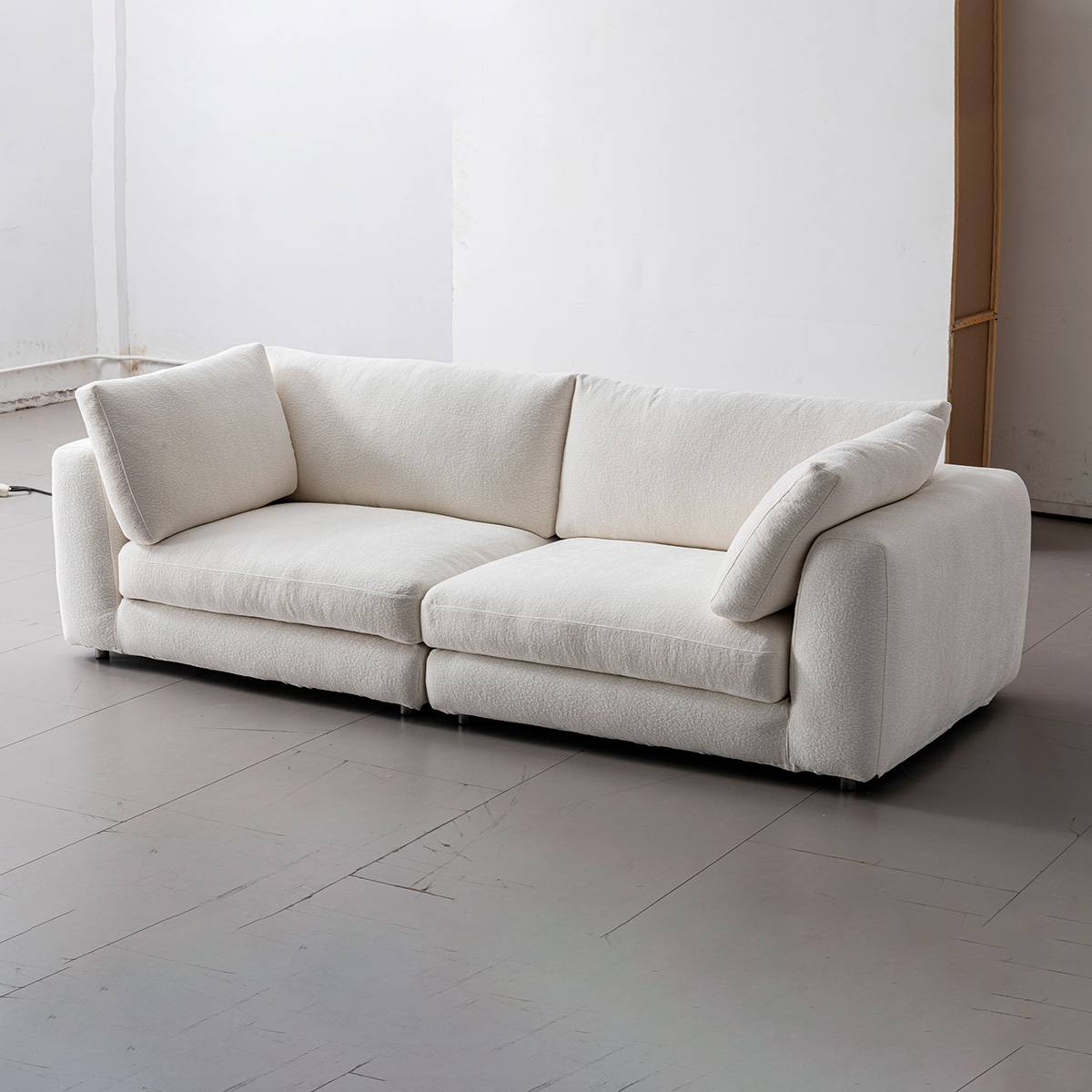 Three-quarter view of the white fabric sofa in a studio setting with wooden flooring.