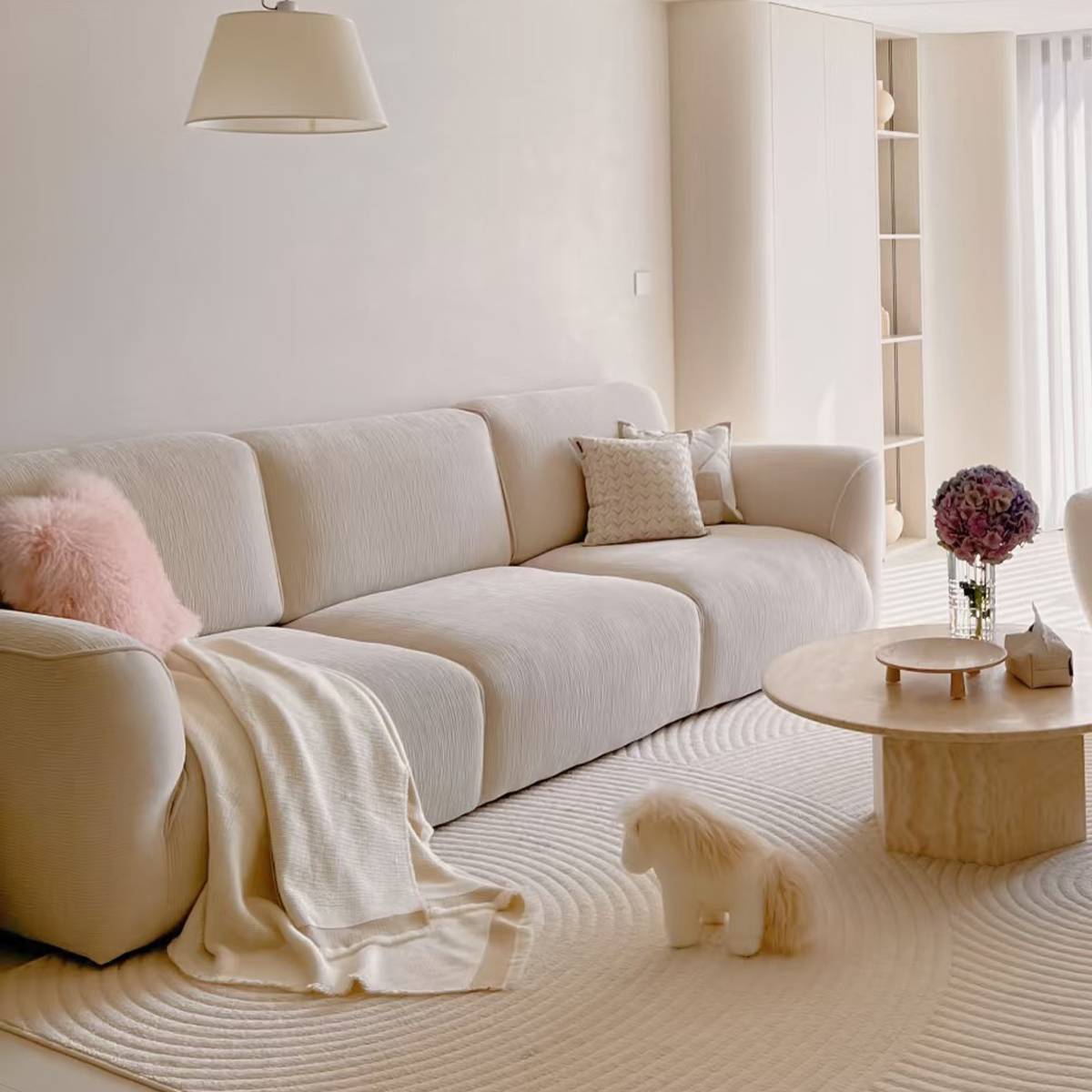 Beige fabric sofa with pink pillow and throw blanket in a bright room