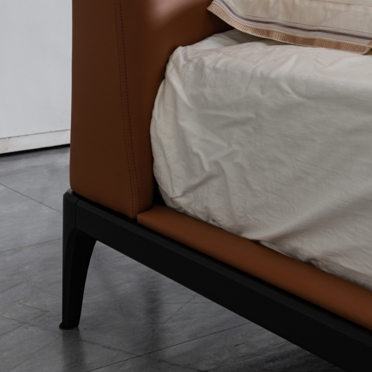 Close-up of the bed frame corner showing the brown leather upholstery and black wooden leg