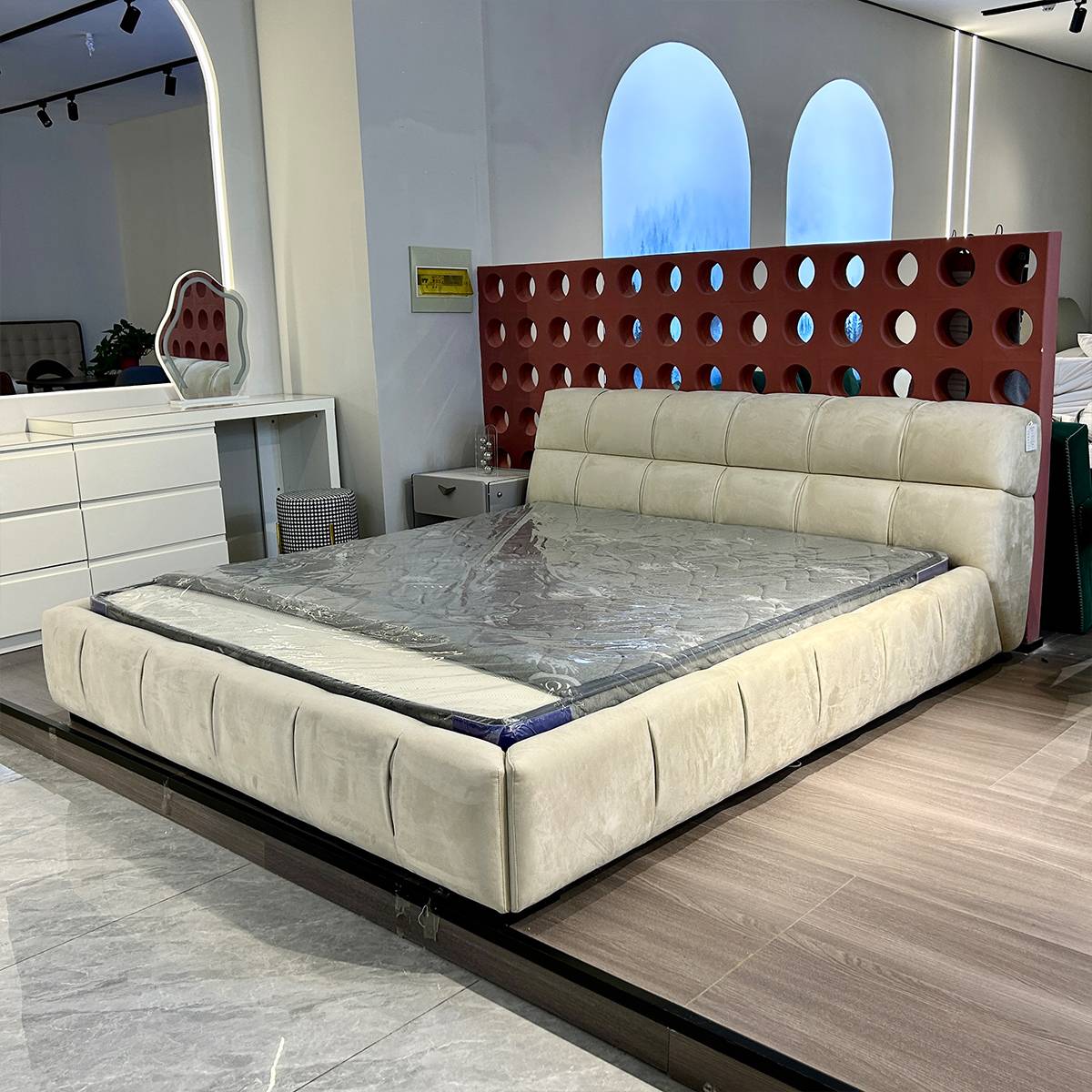 Side view of the beige upholstered puff bed with a red perforated headboard panel behind it