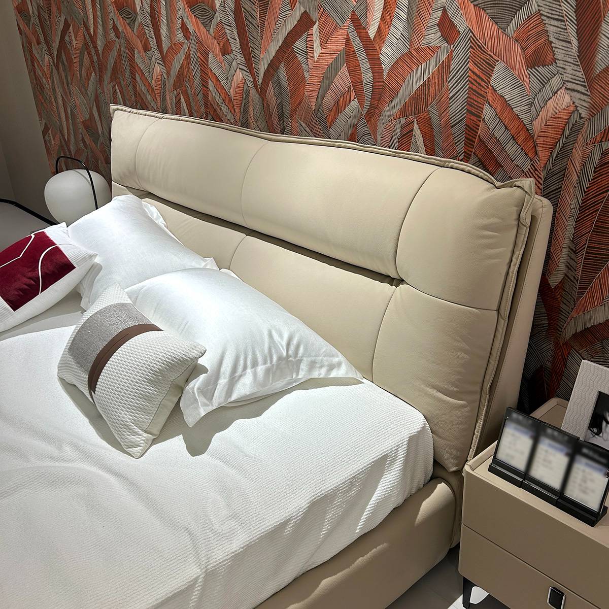 Close-up view of a beige top-grain leather bed headboard with white bedding and a patterned wall background