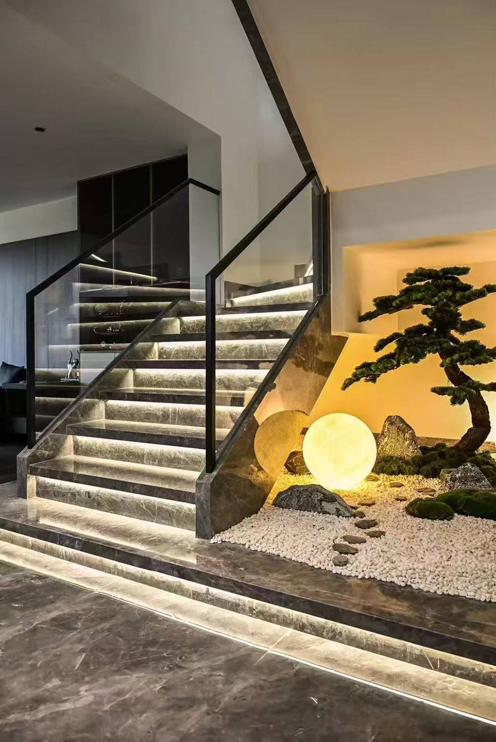 Interior view of a marble staircase with LED lighting and a Zen garden entryway featuring a bonsai tree