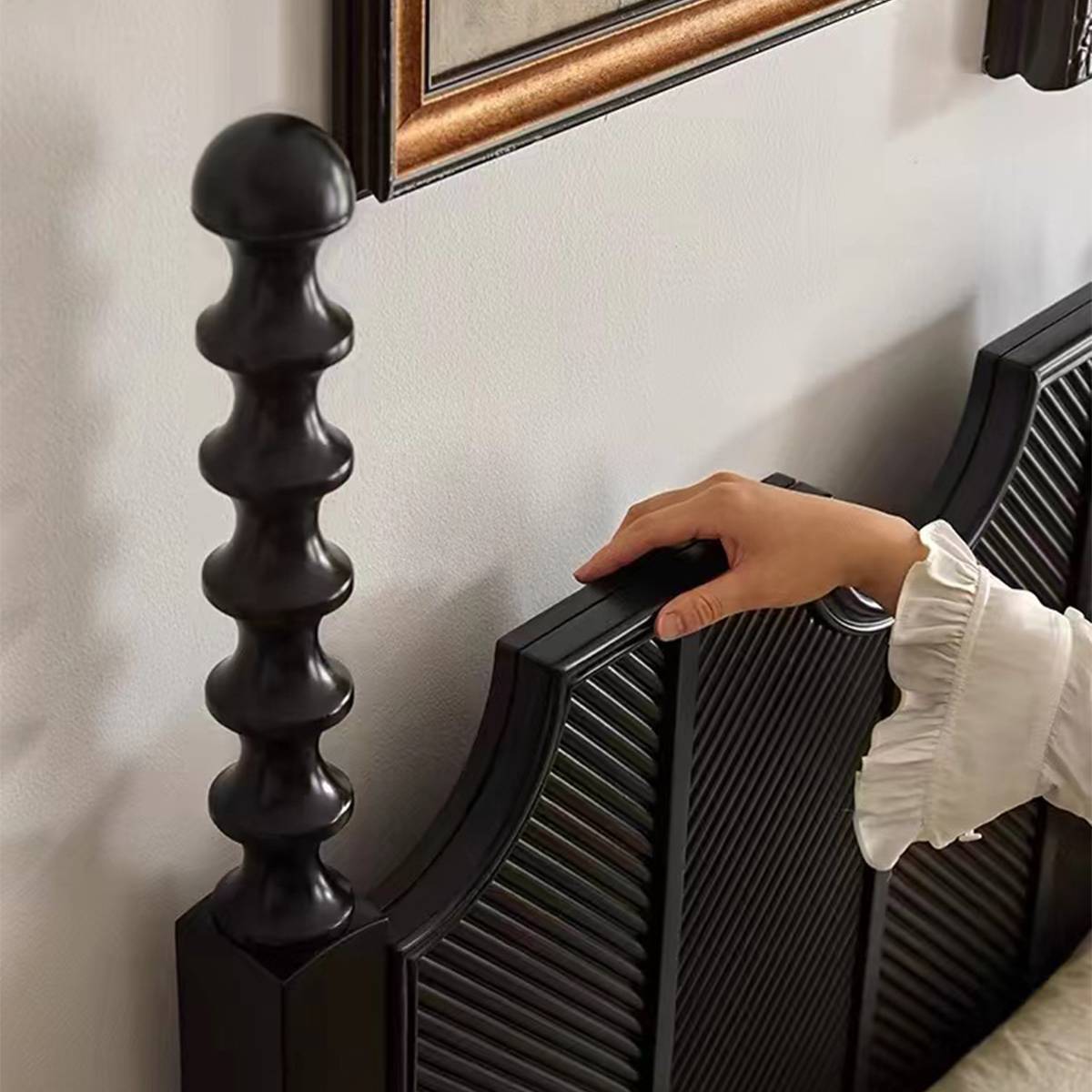Close-up detail of the minimalist black bed's turned post and headboard edge.
