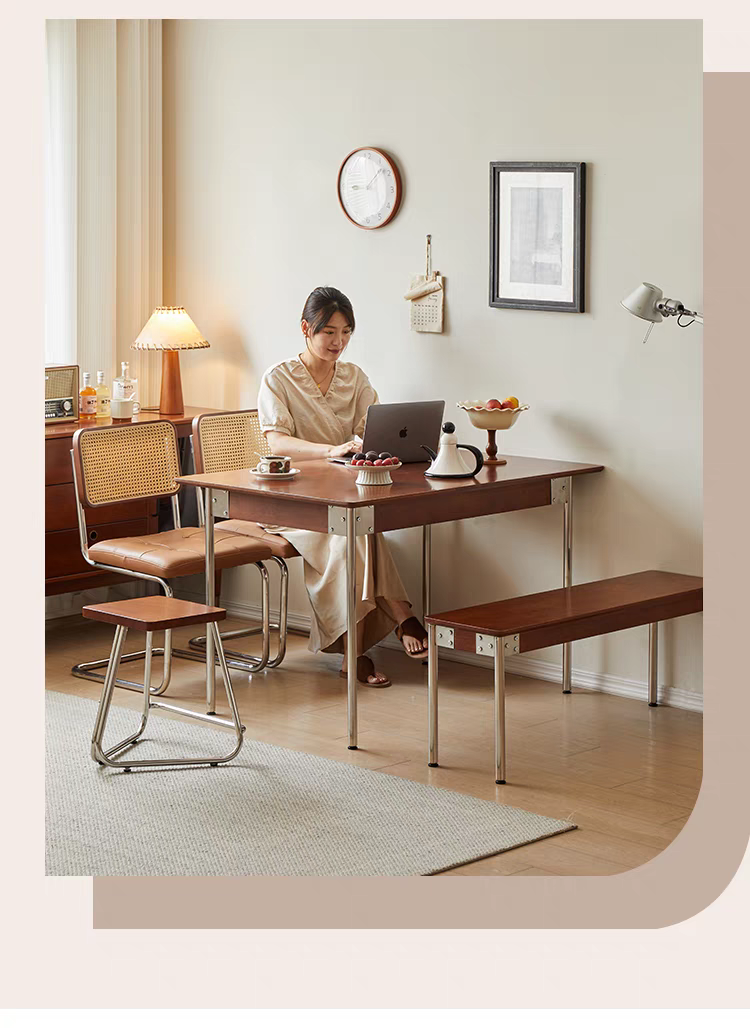 Woman working on a laptop at a wooden dining table with metal legs in a bright room