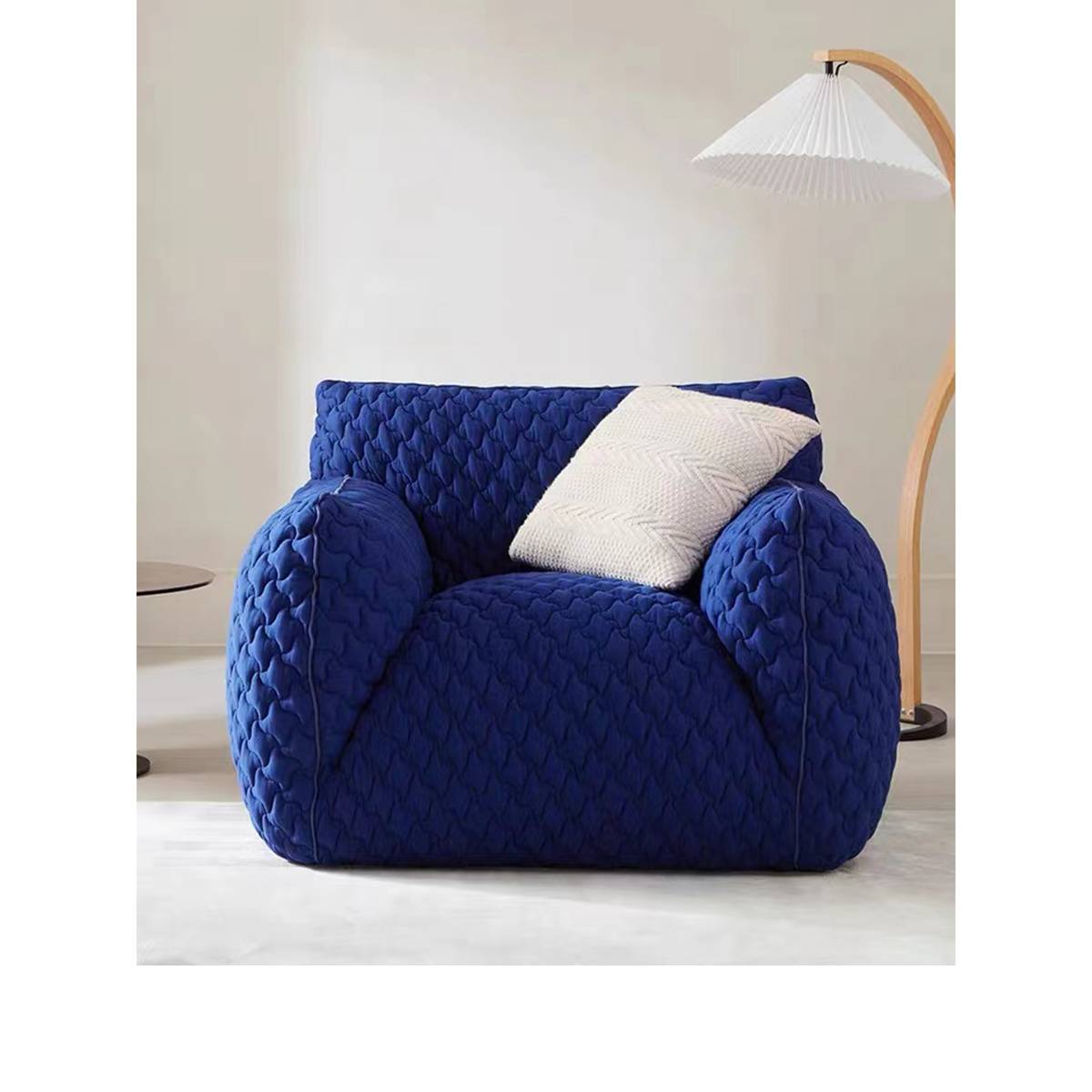 Front view of the blue quilted lounge chair with a white pillow and floor lamp