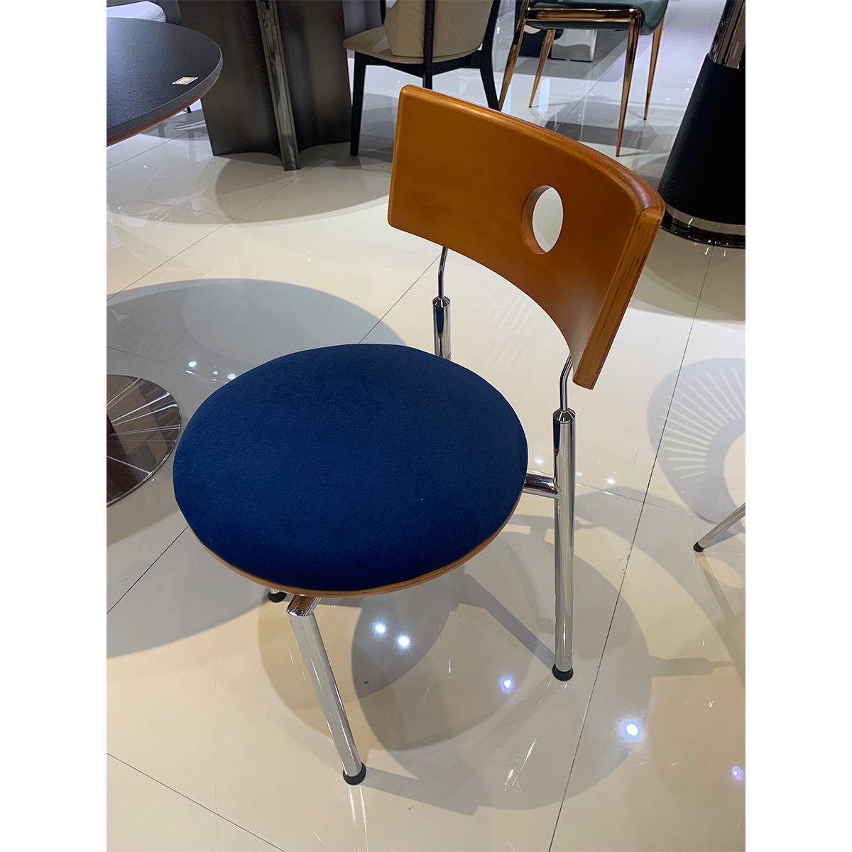 Close-up view of the chair showing the chrome legs and blue upholstery in a showroom setting