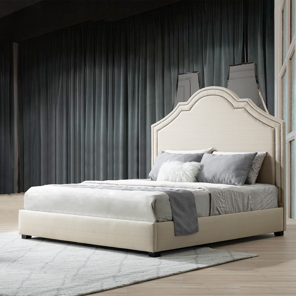 The upholstered bed styled in a bedroom setting with grey curtains and a rug