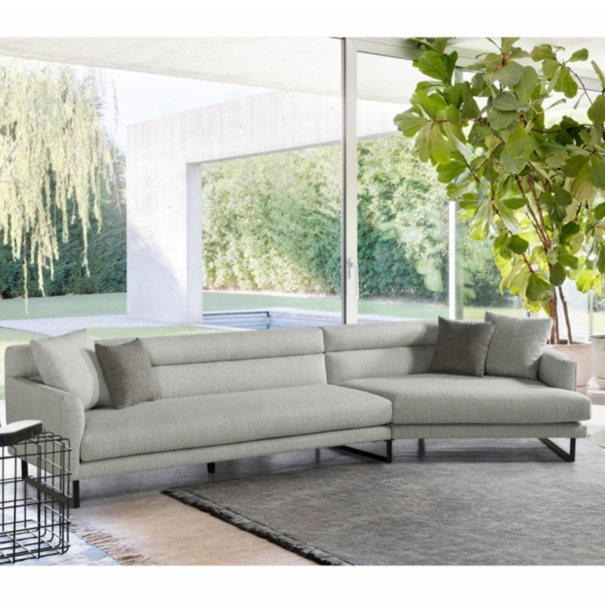 Full view of the grey irregular sofa in a modern living room setting with large windows.