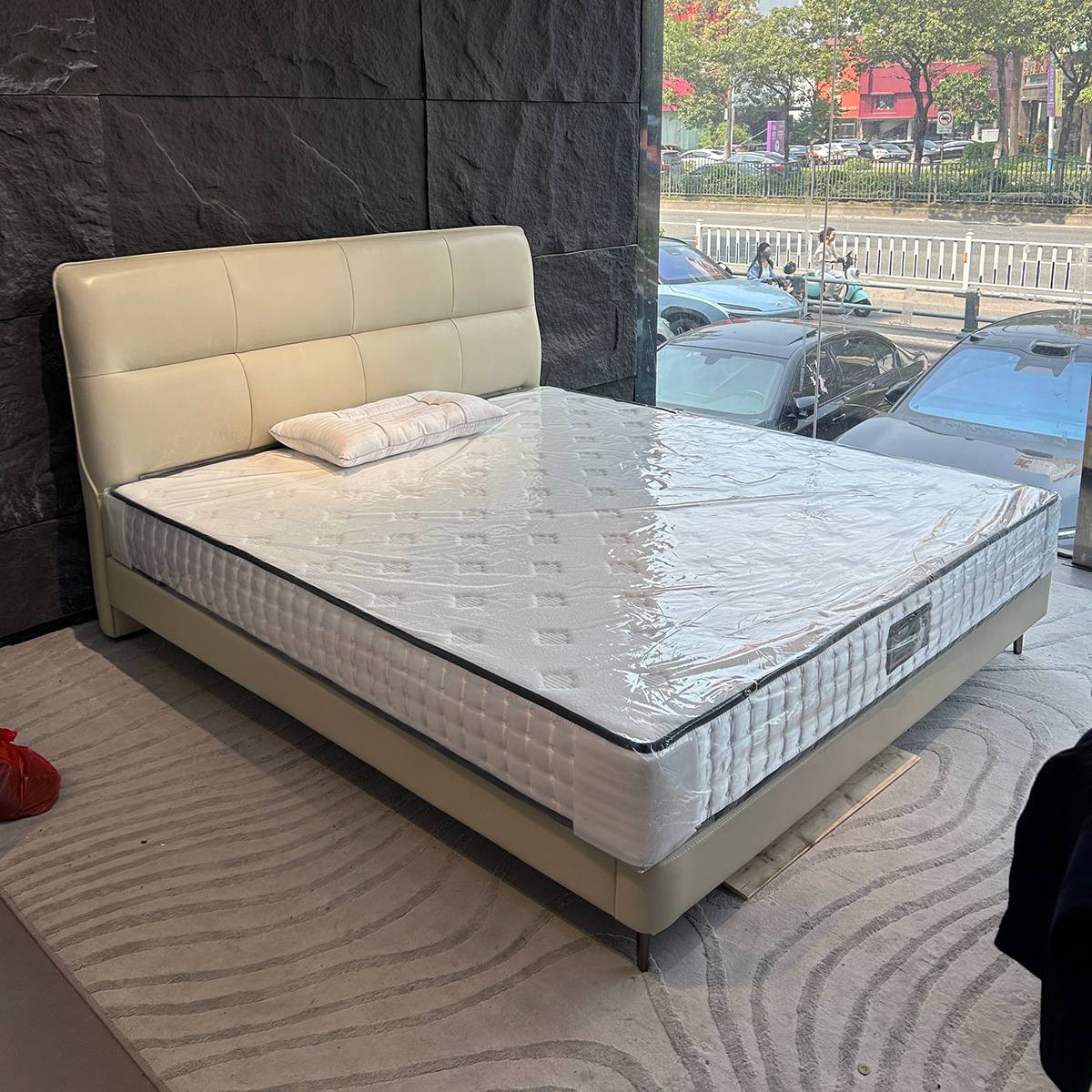 Beige leather bed frame with a mattress wrapped in plastic in a showroom setting