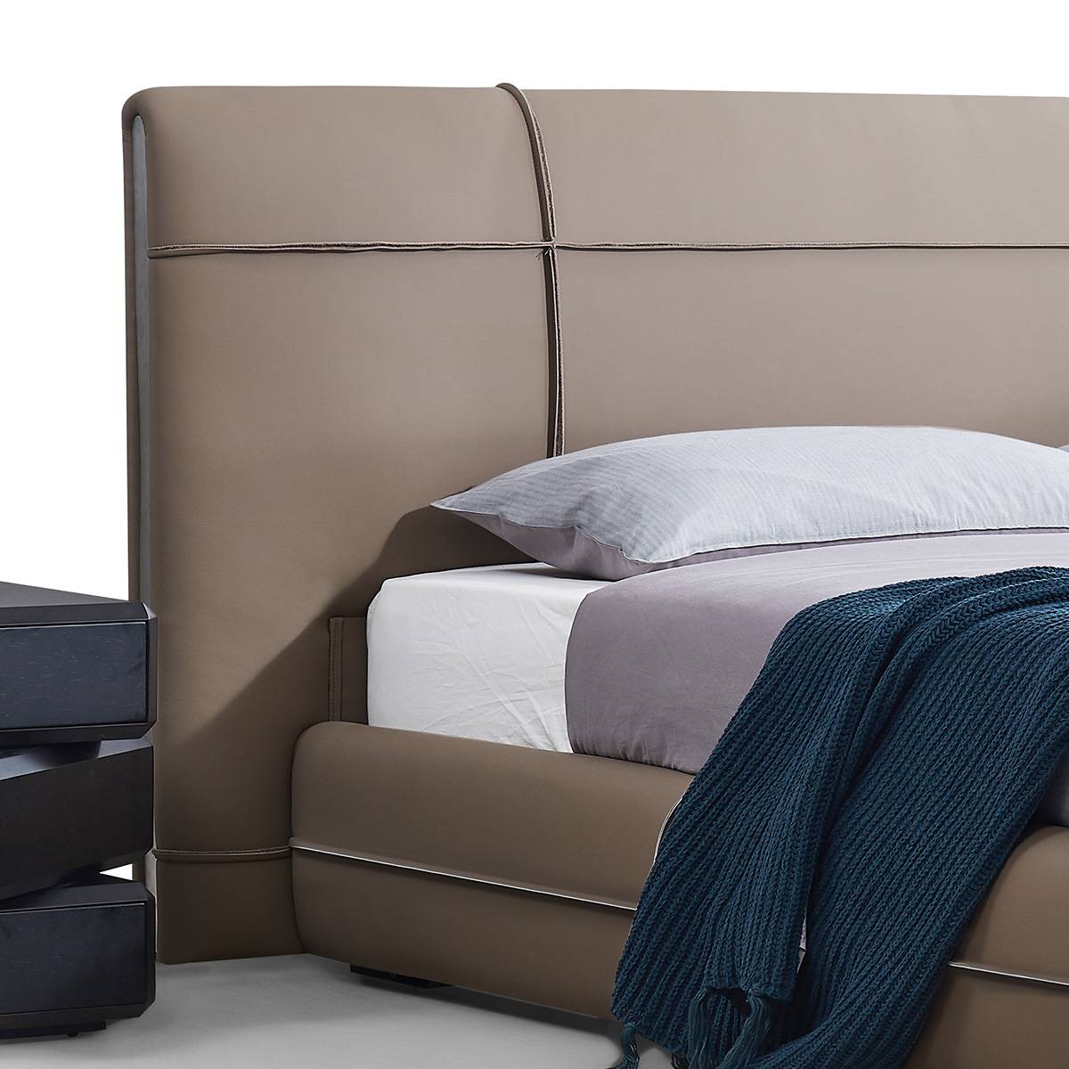 Close-up view of a taupe leather bed with a tall headboard featuring geometric stitching, styled with white and grey bedding and a blue throw.