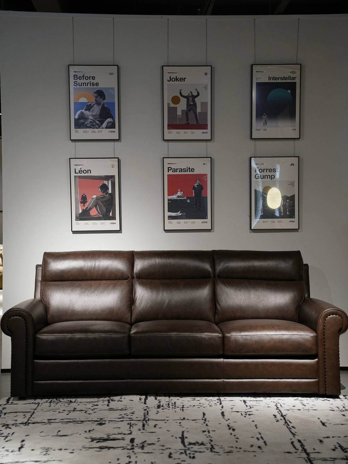 The brown leather sofa displayed in a living room setting with movie posters on the wall.