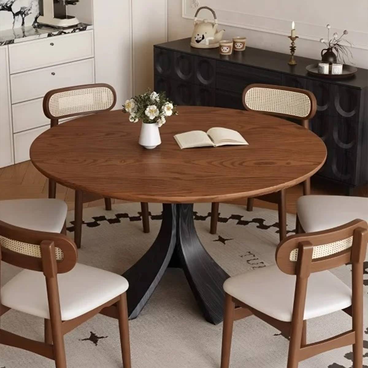 Close-up of the round dining table with a lighter walnut finish and cane-back chairs, styled with a vase and book.