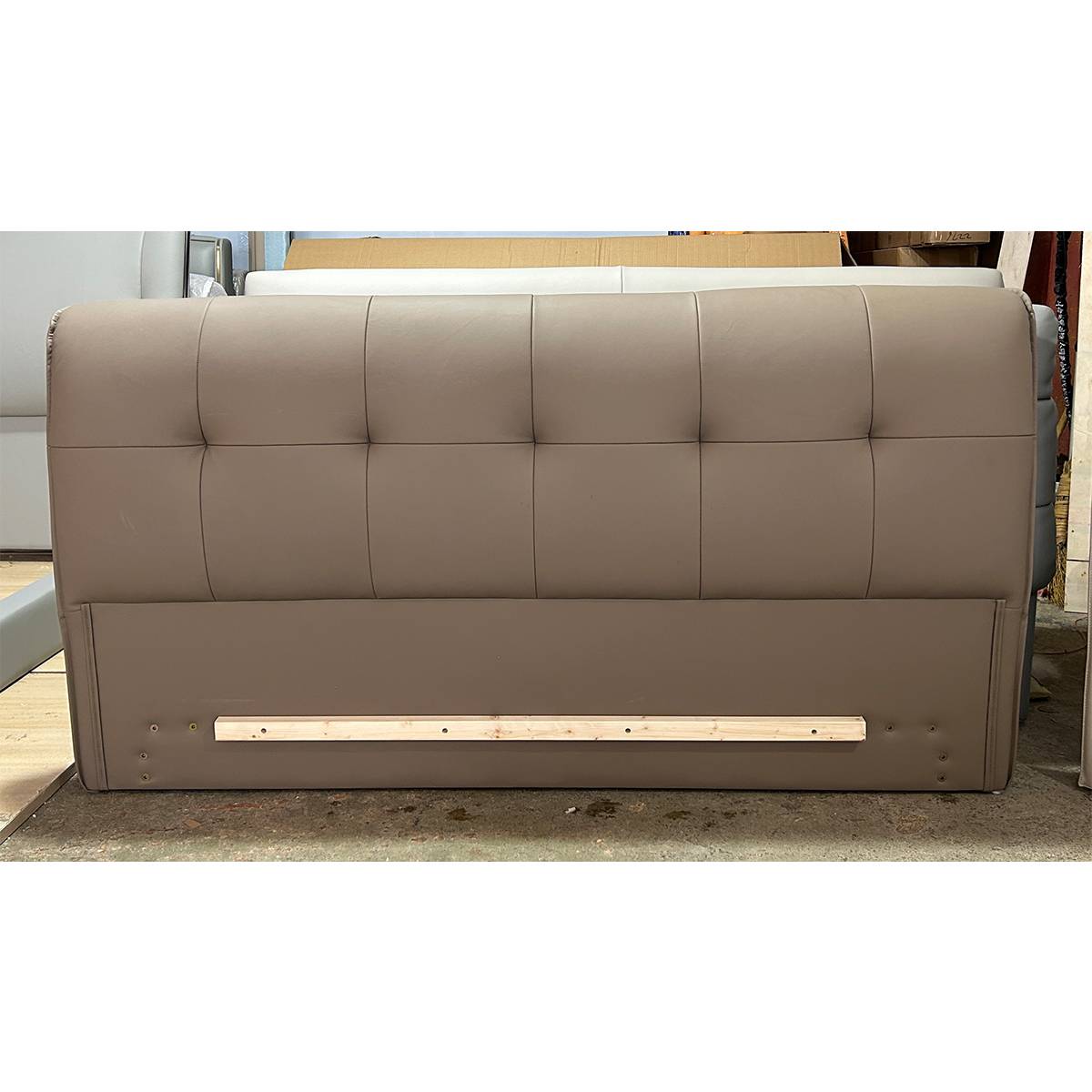 Rear view of a taupe tufted leather bed headboard showing the wooden support bar and metal leg mounting points