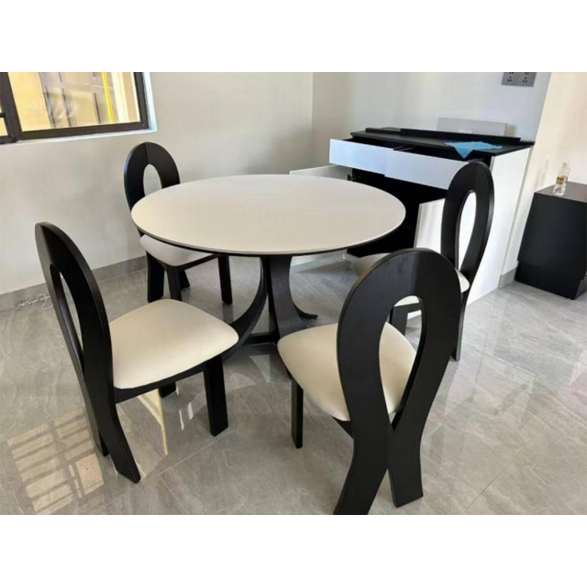 The round dining table set with four matching black chairs in a bright room.
