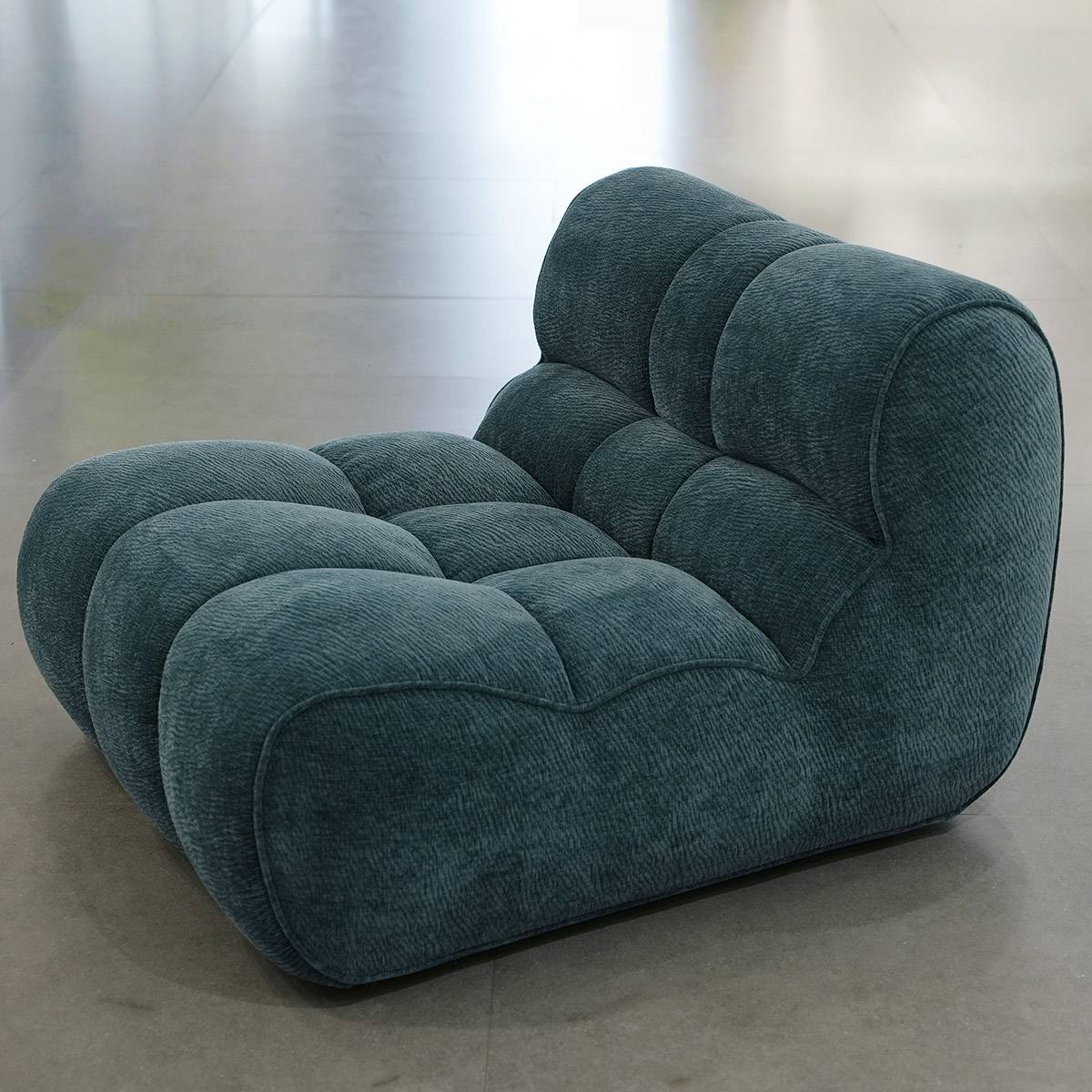 Side angle view of the teal lounge chair on a grey floor
