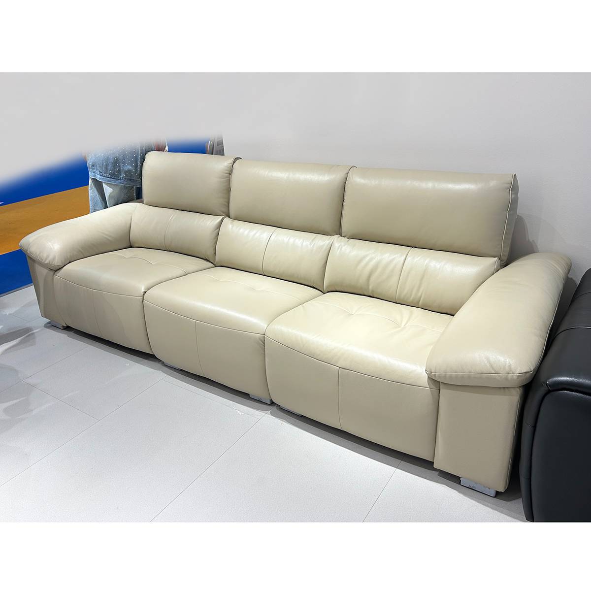 Side view of a beige leather functional sofa in a living room setting with a woman reclining on the left seat.