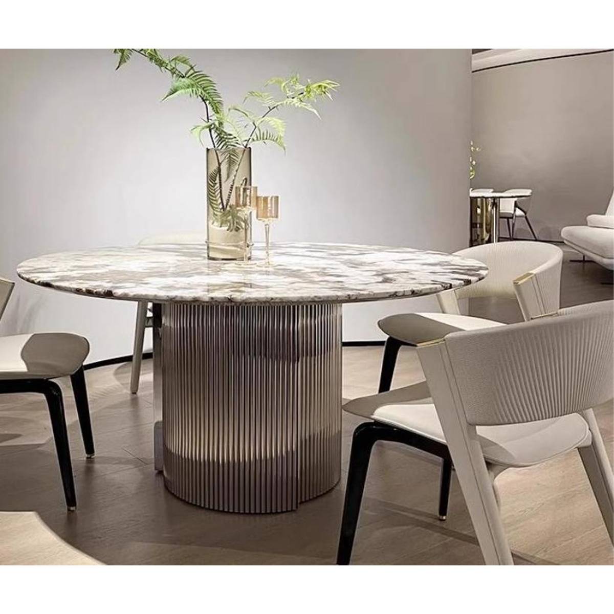Side view of the round dining table showing the fluted stainless steel base and dining chairs.