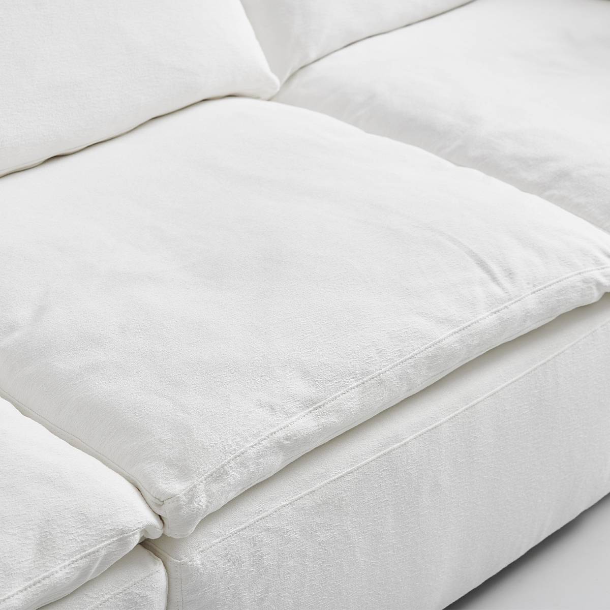 Close-up view of the white fine linen fabric texture and stitching on the Cloud Sofa cushions.