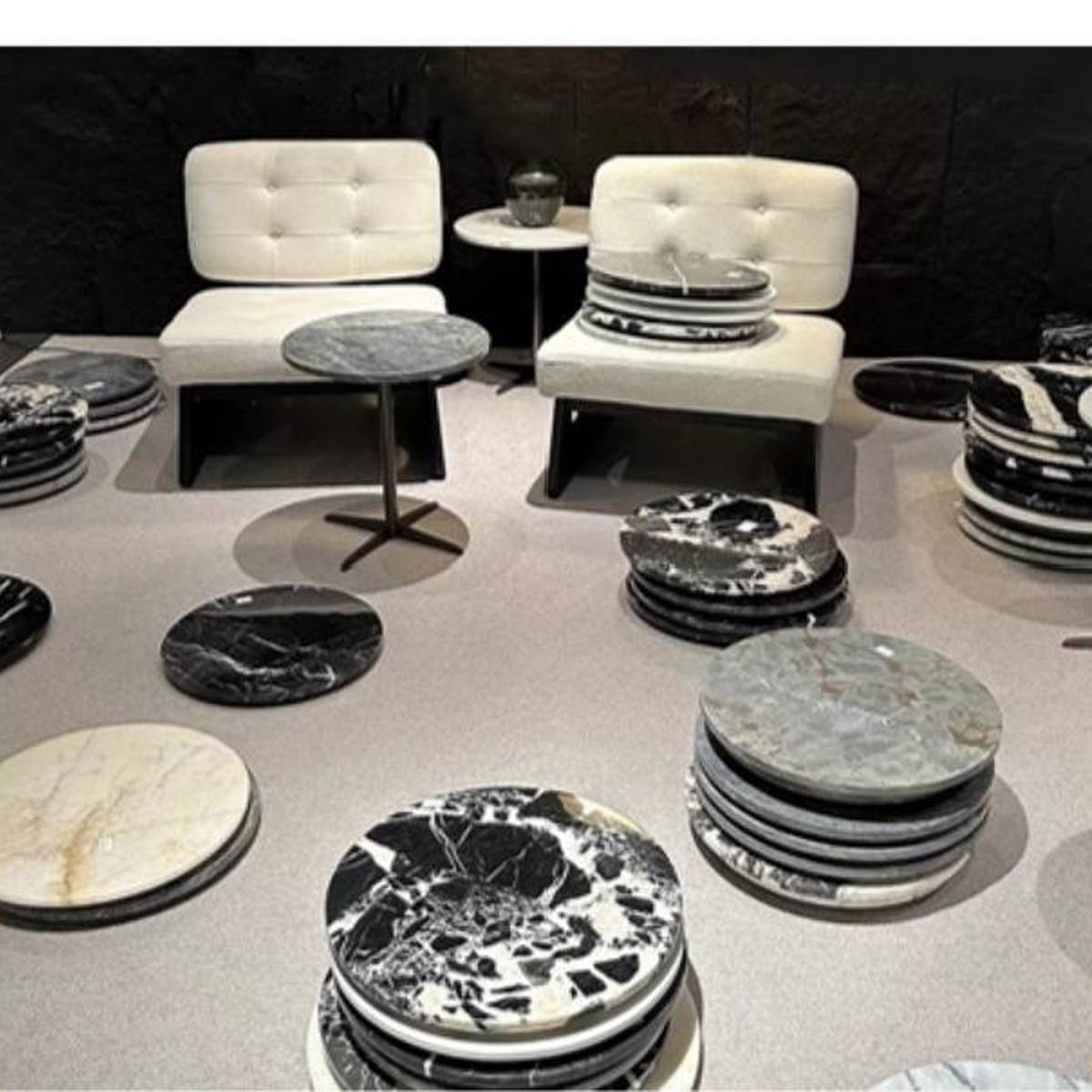 Showroom display of various marble table tops and side tables with white chairs