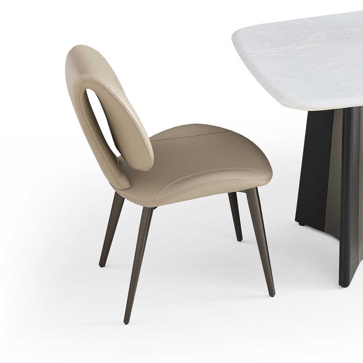Side view of a beige faux leather dining chair with a cutout backrest and dark metal legs next to a marble table