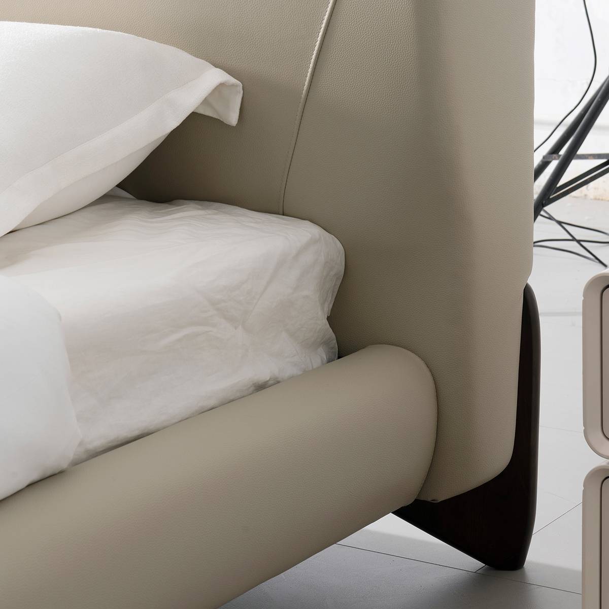 Close-up detail of the bed frame corner showing leather texture and dark wooden leg