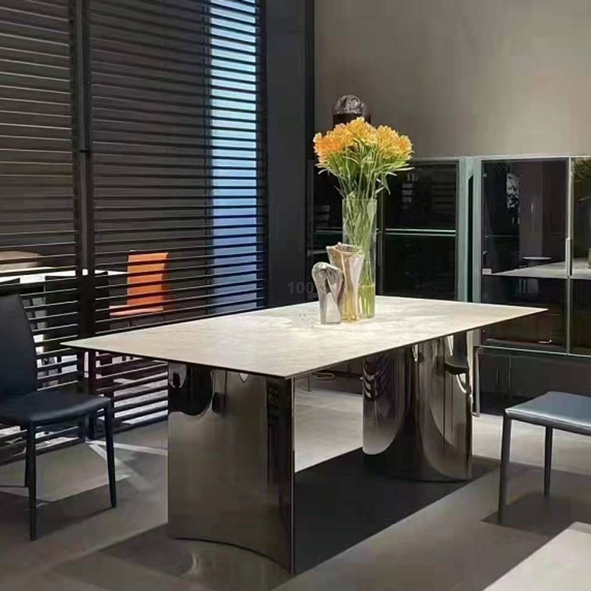 Side view of the dining table with a light marble top and stainless steel base, featuring a vase of yellow flowers.