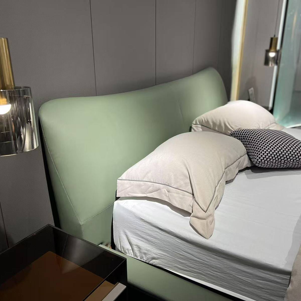 Close-up view of a light green leather bed with a curved headboard, white bedding, and a black and white patterned pillow.